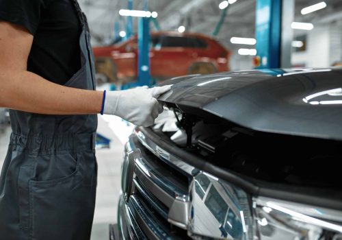 Male mechanic closes the hood, car service. Vehicle repairing garage, man in uniform, automobile station interior on background