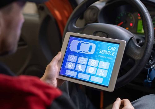 Young repairman with digital tablet sitting in front of steer and looking at icons and options on home page of car service website on screen